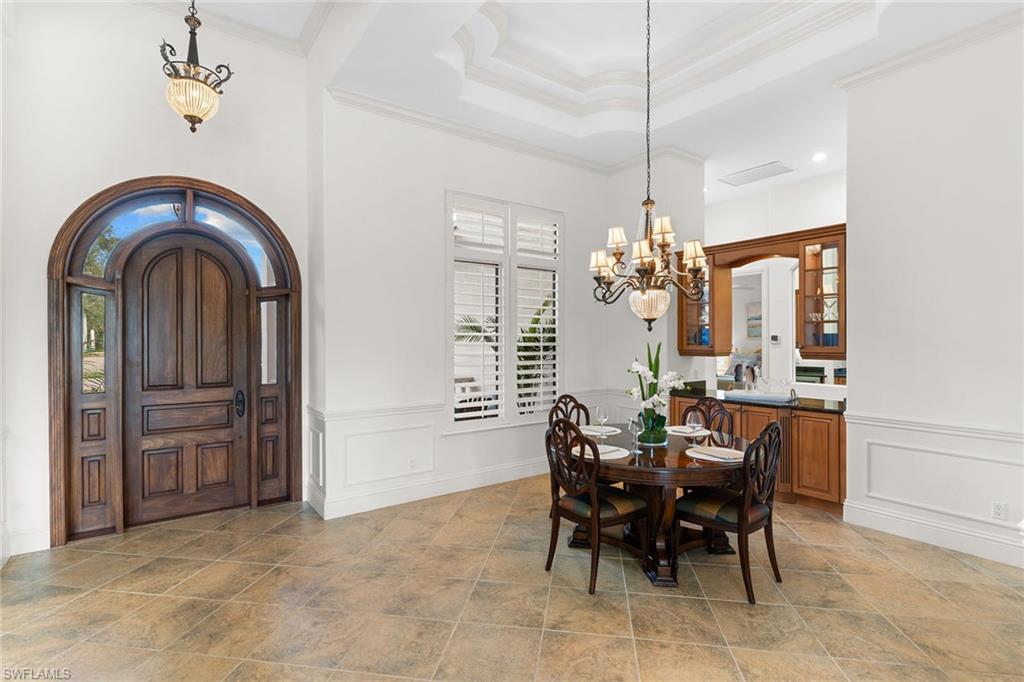 7506 Hogan Court Naples, FL 34113 - Photo 40 of 49 Dining room with suspended lighting, arched walkways, ornamental molding, a raised ceiling, and light stone finish floors