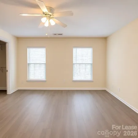an empty room with wooden floor chandelier fan and windows