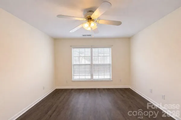 an empty room with wooden floor chandelier fan and windows