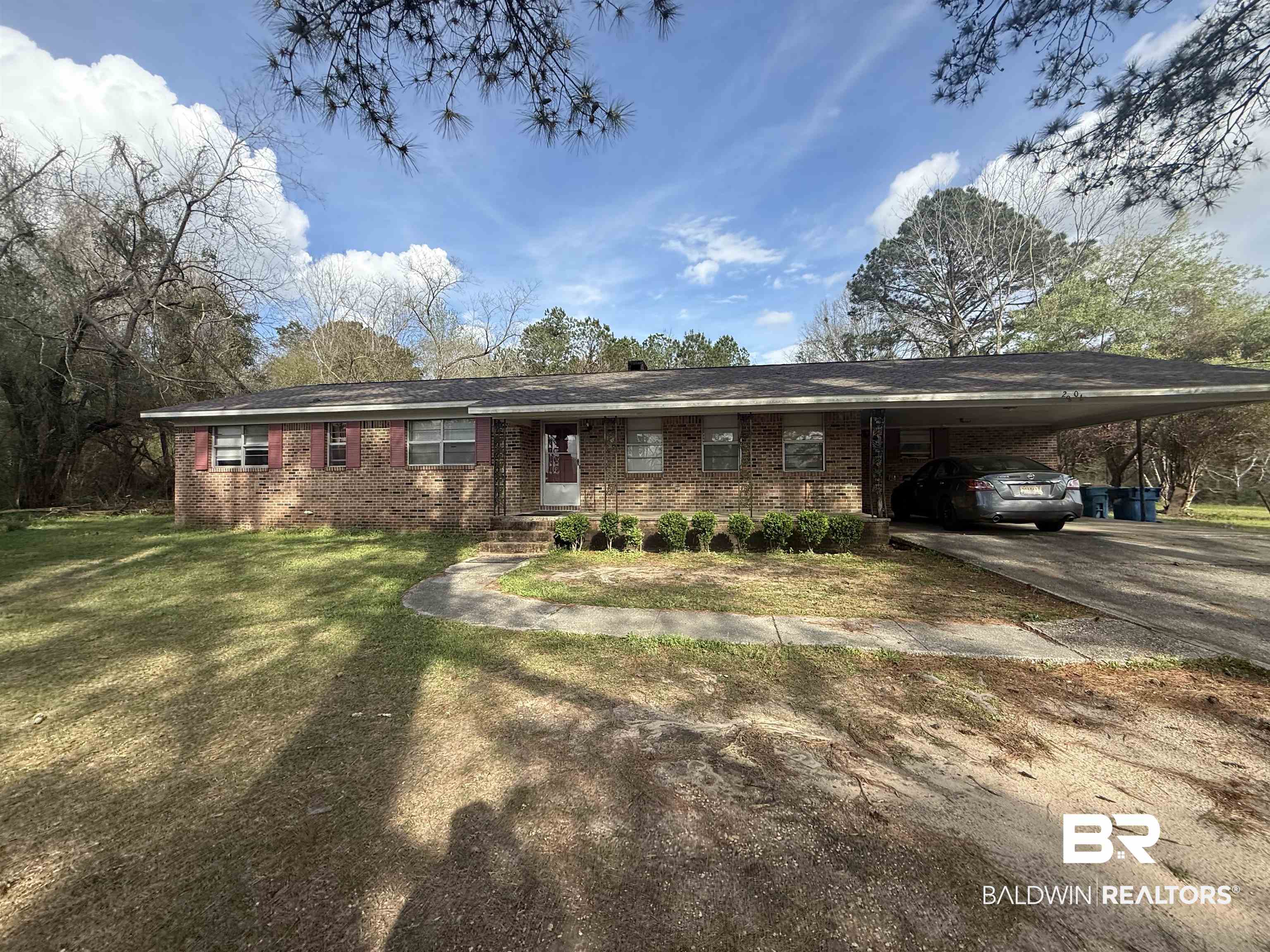 Single story home featuring an attached carport, brick siding, driveway, and a front yard