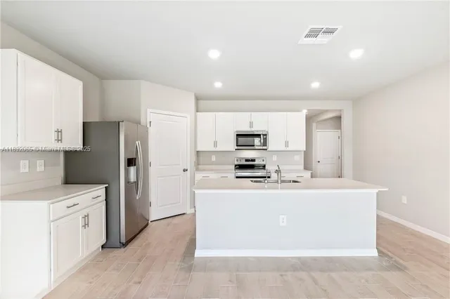 a kitchen with stainless steel appliances a stove top oven a refrigerator a sink a oven with white cabinets