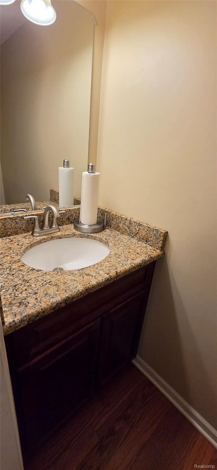 380 Huntington Court Rochester, MI 48307 - Photo 13 of 26 Granite countertop with an integrated sink, dark wood-finish vanity, brushed nickel faucet, and wood-finish flooring