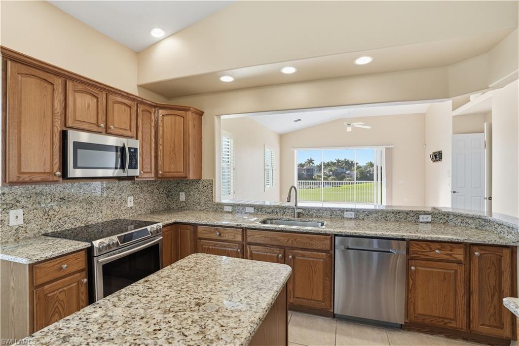 5963 Trophy Drive, Unit 2003 Naples, FL 34110 - Photo 28 of 50 Kitchen featuring vaulted ceiling, brown cabinetry, appliances with stainless steel finishes, light stone counters, and tasteful backsplash
