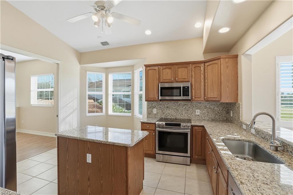 5963 Trophy Drive, Unit 2003 Naples, FL 34110 - Photo 29 of 50 Kitchen featuring light stone countertops, stainless steel appliances, light tile patterned floors, backsplash, and brown cabinetry