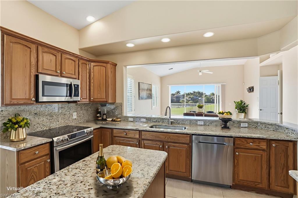 5963 Trophy Drive, Unit 2003 Naples, FL 34110 - Photo 4 of 50 Kitchen with vaulted ceiling, brown cabinetry, appliances with stainless steel finishes, light stone countertops, and tasteful backsplash