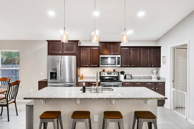 a kitchen with stainless steel appliances granite countertop a sink a stove a refrigerator cabinets and chairs