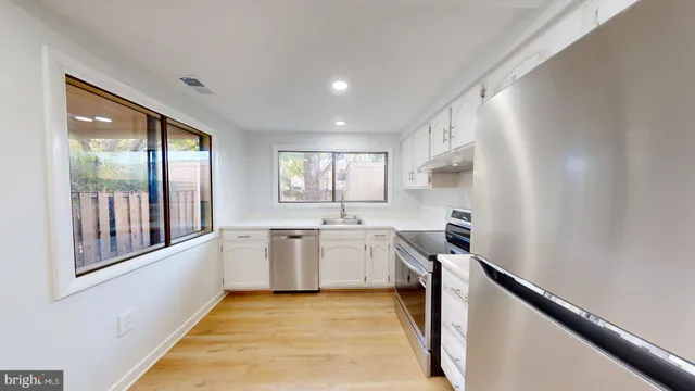 a large white kitchen with wide window and refrigerator