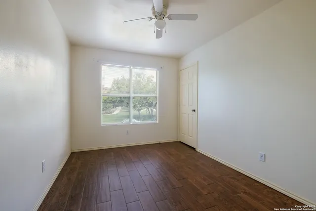 an empty room with wooden floor chandelier fan and windows