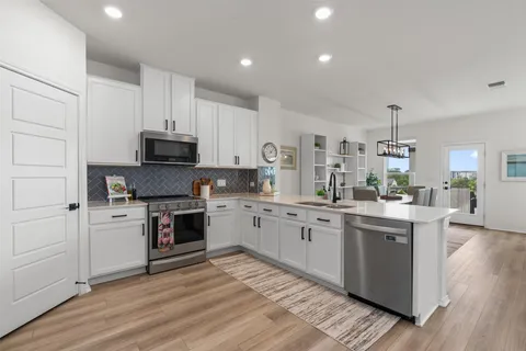 a kitchen with stainless steel appliances granite countertop a stove top oven a sink dishwasher and a refrigerator with wooden floor