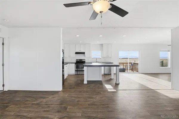a kitchen with stainless steel appliances kitchen island granite countertop a refrigerator a stove and white cabinets with wooden floor