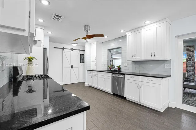 a kitchen with stainless steel appliances a sink dishwasher a refrigerator and white cabinets with wooden floor