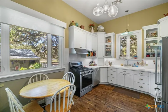 a kitchen with stainless steel appliances granite countertop a stove a sink dishwasher a dining table and chairs with wooden floor