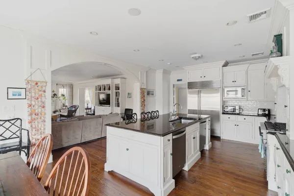 a kitchen with stainless steel appliances granite countertop a stove top oven a sink a dining table and chairs with wooden floor