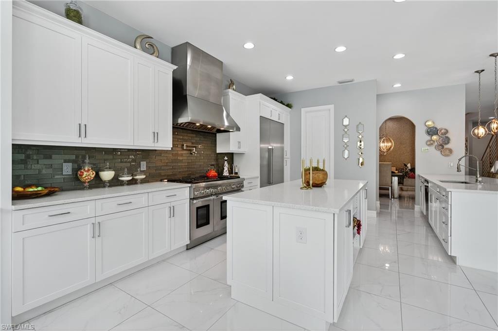 14690 Reserve Place Naples, FL 34109 - Photo 15 of 48 Kitchen with white cabinets, wall chimney range hood, a large island, high end appliances, and tasteful backsplash