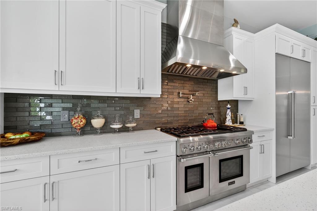 14690 Reserve Place Naples, FL 34109 - Photo 16 of 48 Kitchen featuring wall chimney exhaust hood, high end appliances, decorative backsplash, and white cabinets