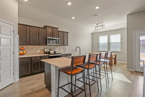 a kitchen with stainless steel appliances granite countertop a stove a sink a microwave a dining table and chairs with wooden floor