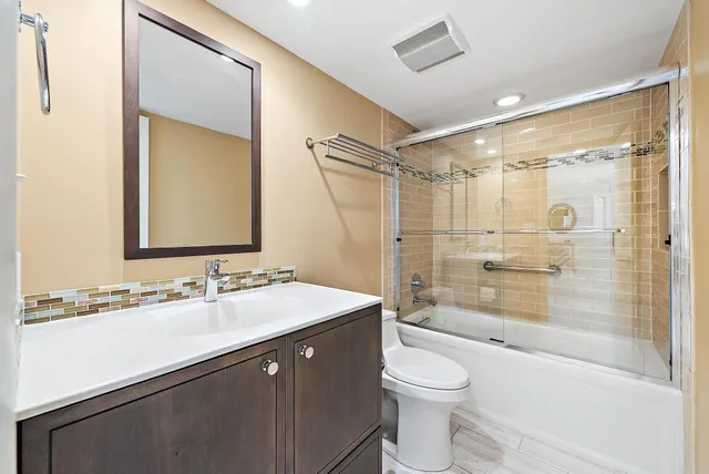 a bathroom with a bathtub shower sink vanity mirror and toilet