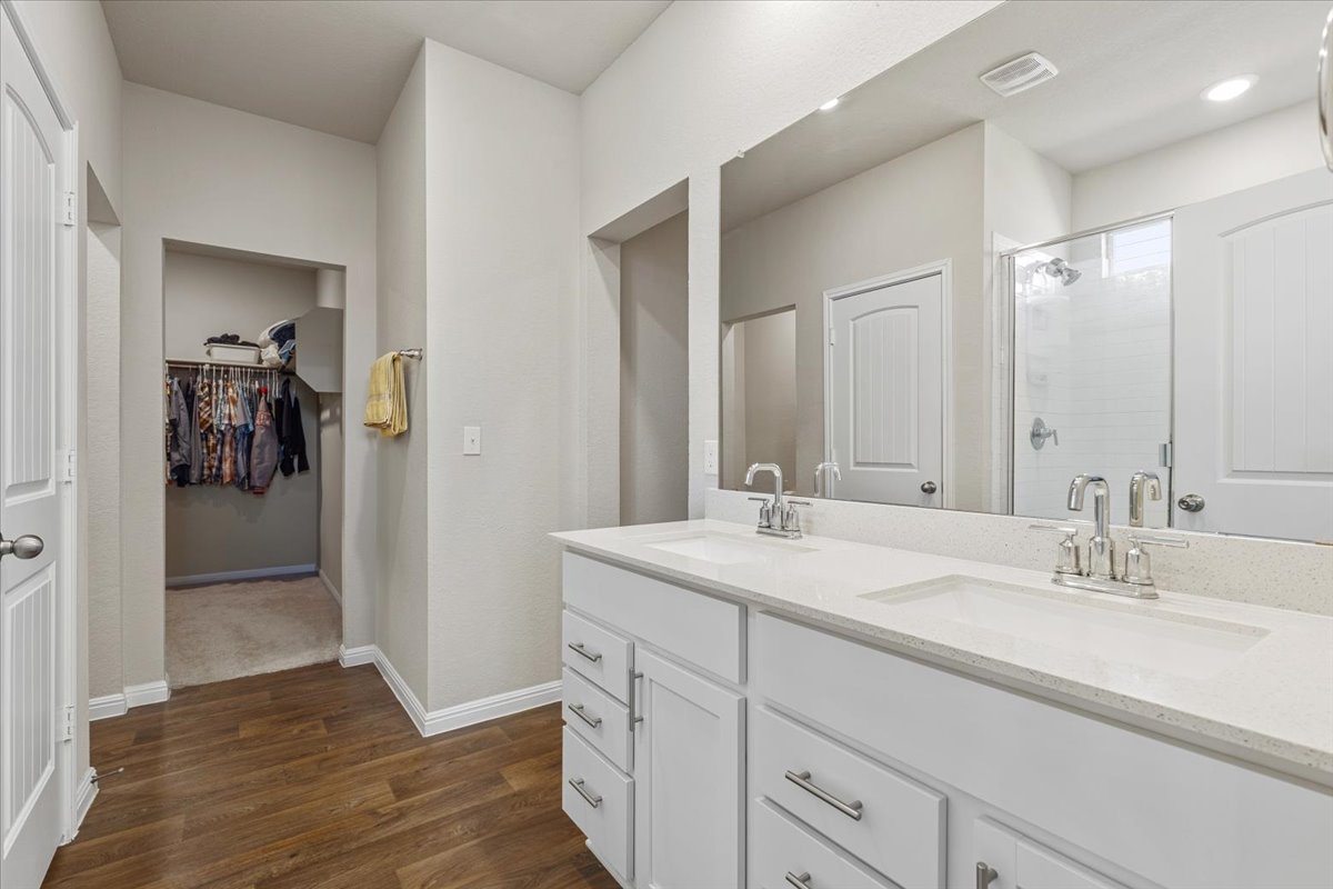 112 Rainmaker Cove Bastrop, TX 78602 - Photo 19 of 34 Bathroom featuring double vanity, a shower stall, a spacious closet, and dark wood-style flooring