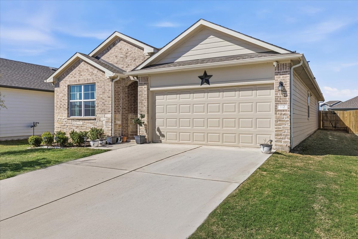 112 Rainmaker Cove Bastrop, TX 78602 - Photo 2 of 34 Ranch-style house with stone siding, a garage, and driveway