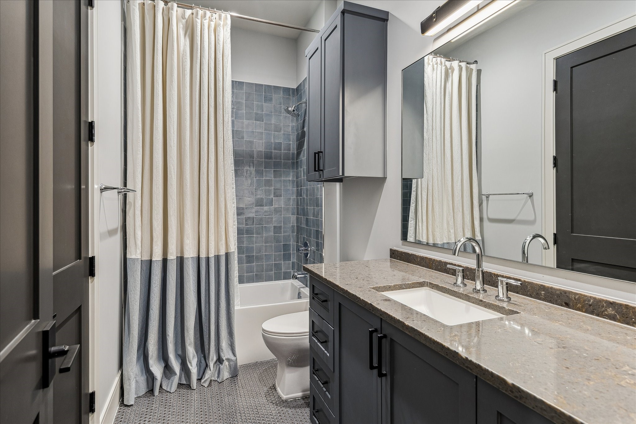 3807 Westerman Street Houston, TX 77005 - Photo 39 of 50 Guest Bathroom 3, accessible from Bedroom 3 and the hallway to the game room, features penny tile flooring and neutral designer wall paint. An acrylic tub/shower combination is fitted with polished nickel and matte black Delta hardware, while the vanity includes a white undermount ceramic sink, storage cabinets, and a Delta faucet.