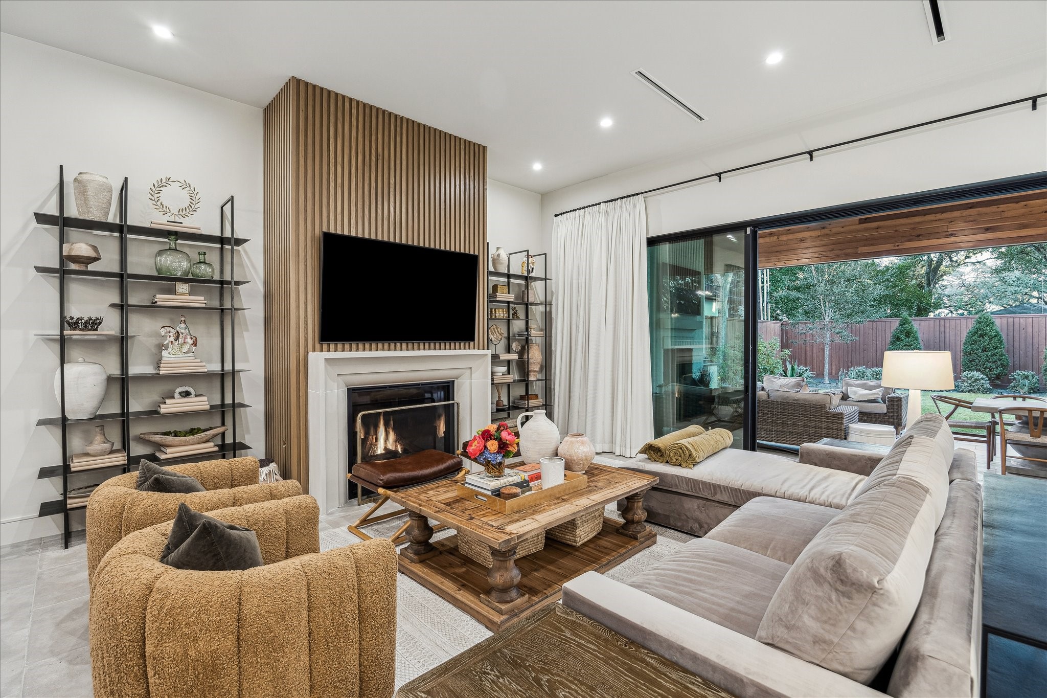 3807 Westerman Street Houston, TX 77005 - Photo 9 of 50 Exuding comfort and style, the family room features neutral designer wall paint and a striking feature wall that anchors the space. Recessed LED lighting and a gas fireplace with a cast stone mantel and fluted wood accents add warmth and sophistication. A large picture sliding door provides serene backyard views, while the open layout connects seamlessly to the dining room and designer kitchen.