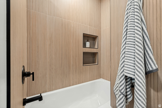 1010 West Maple Street Mapleton, UT 84664 - Photo 13 of 24 Bathroom featuring a white bathtub with matte black fixtures, textured wood-tone tile surround, and two recessed shower niches