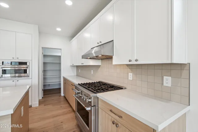 a kitchen with stainless steel appliances granite countertop a refrigerator a sink dishwasher a stove and white countertops with wooden floor