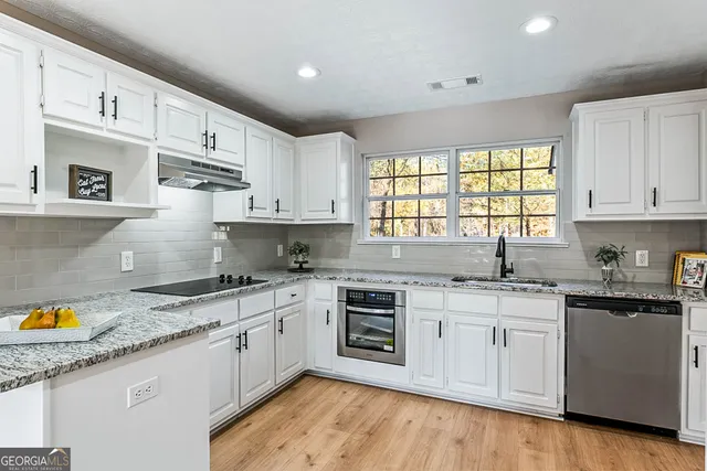a kitchen with stainless steel appliances granite countertop a stove a sink and white cabinets