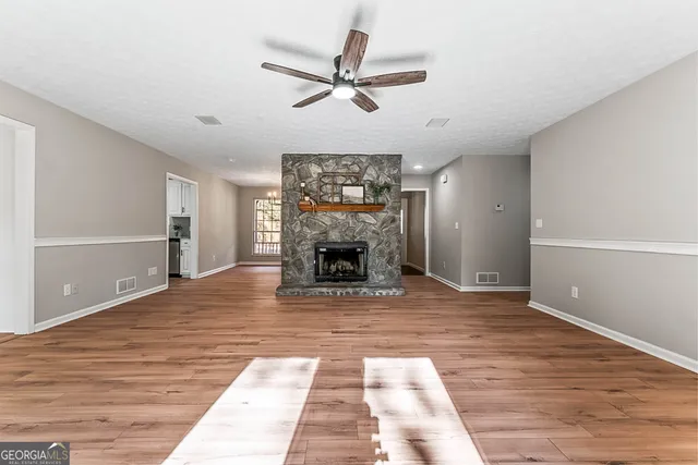a view of a livingroom with a fireplace a ceiling fan and wooden floor