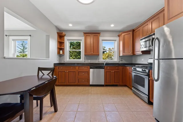 a kitchen with stainless steel appliances granite countertop a stove a sink dishwasher a refrigerator and a dining table with wooden cabinet