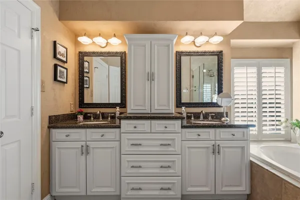 a bathroom with a tub sink vanity granite and shower