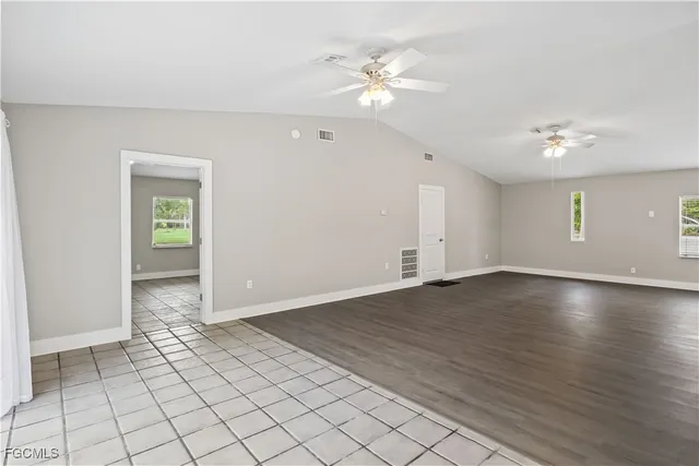 an empty room with wooden floor chandelier fan and windows