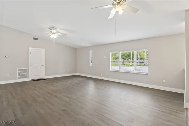 an empty room with wooden floor chandelier fan and windows