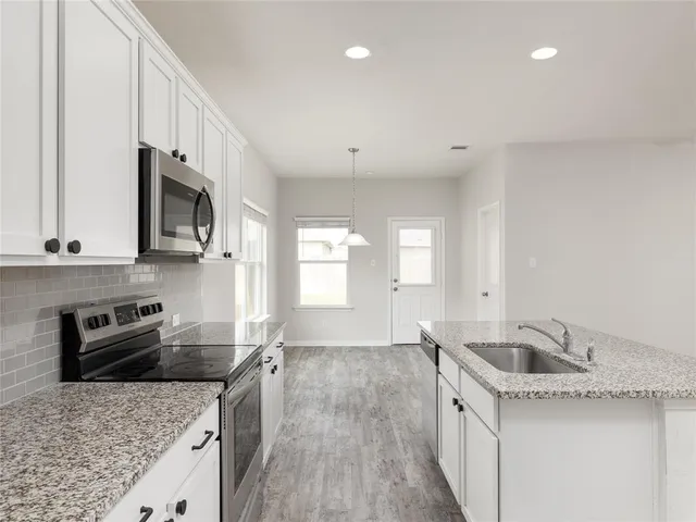 a kitchen with granite countertop a sink a counter space appliances and cabinets