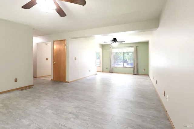 an empty room with chandelier fan and windows