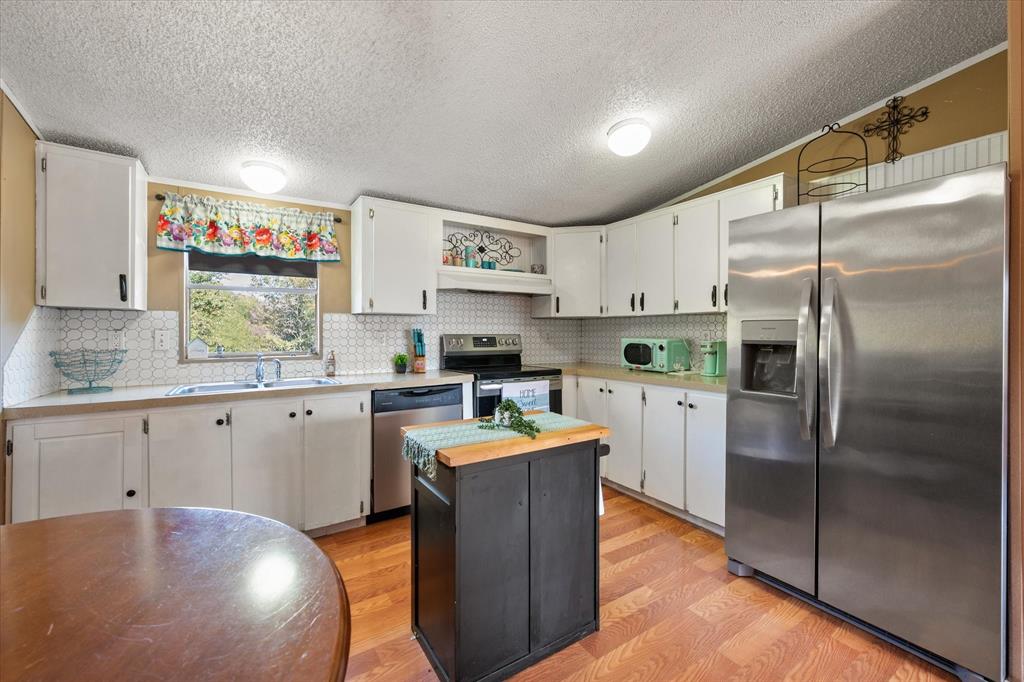 309 Southeast County Road Corsicana, TX 75109 - Photo 10 of 27 White cabinetry with dark hardware, stainless steel appliances, wood-finish flooring, white hexagonal tile backsplash, and a central island with a wood countertop