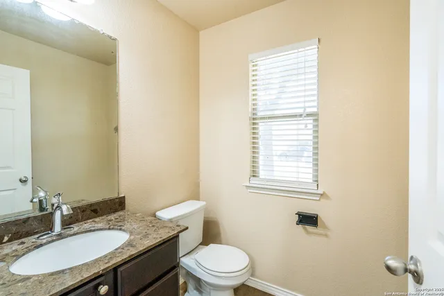 a bathroom with a granite countertop sink toilet a mirror and a window
