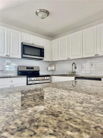 a kitchen with stainless steel appliances granite countertop a stove a sink a microwave a refrigerator and cabinets