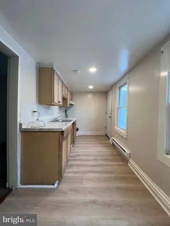 a view of an empty room with kitchen and window