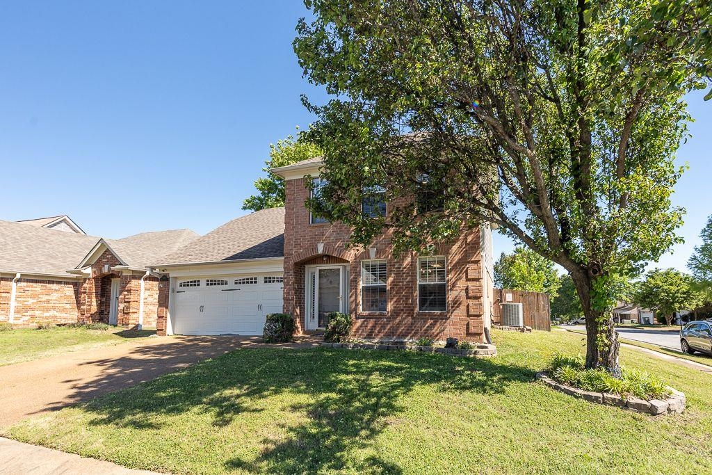 9768 Riggin Drive Memphis, TN 38002 - Photo 28 of 32 Brick exterior featuring a two-car garage, mature trees, and a landscaped front yard