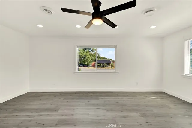 an empty room with wooden floor fan and windows