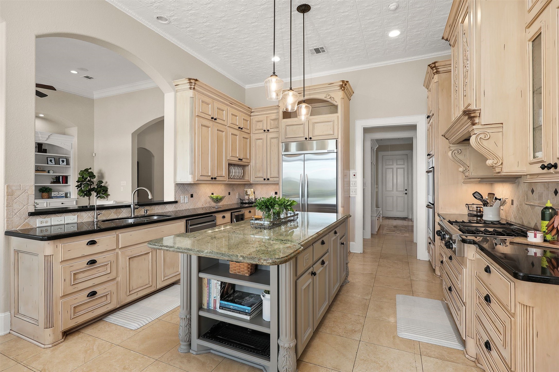 10896 Decatur Street Willis, TX 77318 - Photo 28 of 50 Discover a chef's dream kitchen with custom wood cabinetry, a spacious granite island, and stainless steel appliances, seamlessly flowing into a cozy living area with tiled flooring and a soothing neutral palette, all accentuated by elegant pendant lighting.