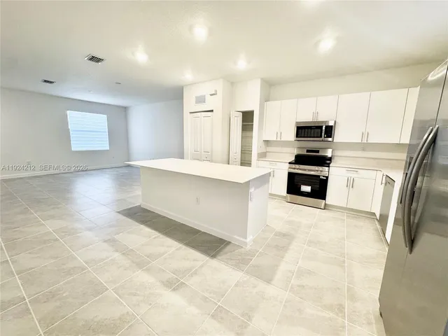 a large kitchen with kitchen island granite countertop a refrigerator a sink a stove a microwave a counter space and cabinets