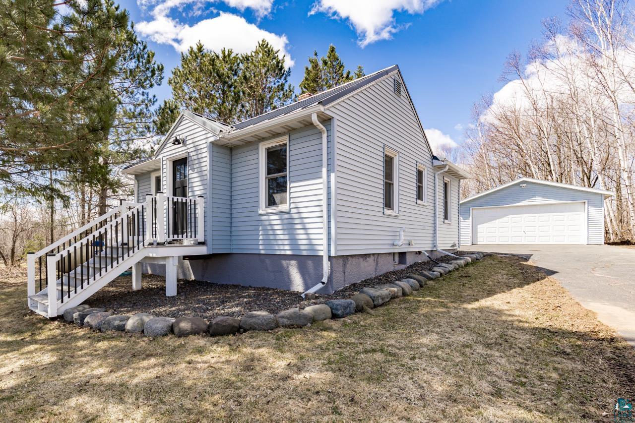 3645 Haines Road Hermantown, MN 55811 - Photo 10 of 35 Light blue siding exterior featuring white trim, a front entry deck with white railings and black balusters, and a detached two-car garage with a paved driveway