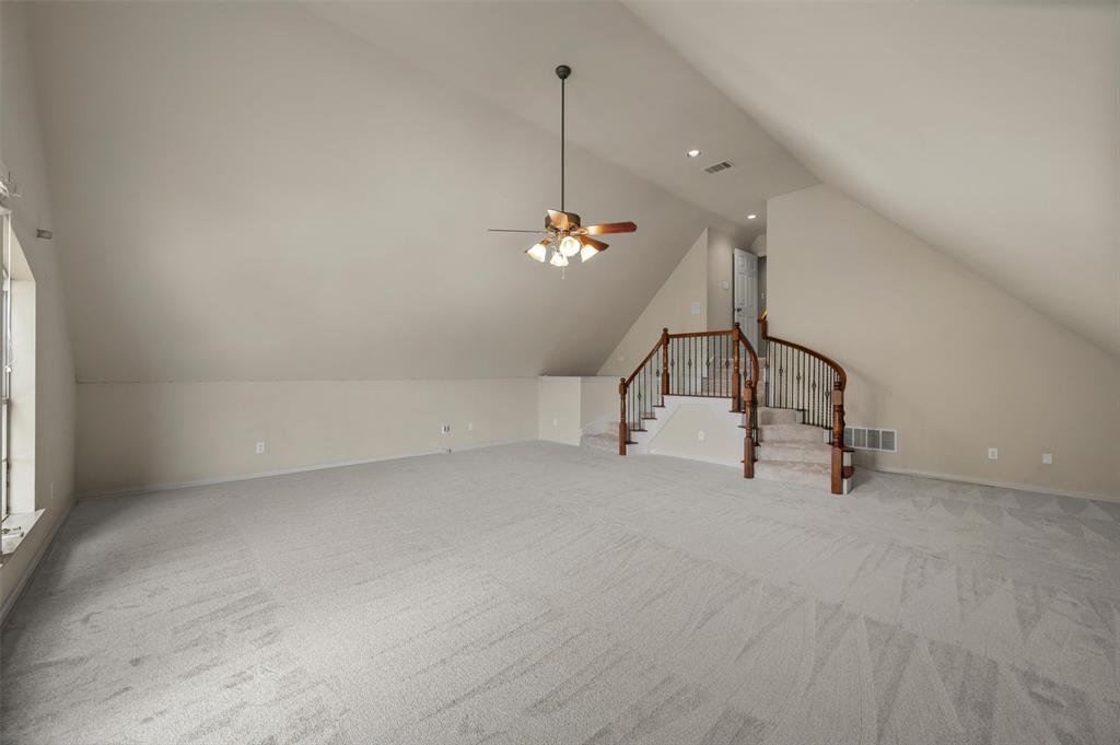 5607 Ranger Drive Rockwall, TX 75032 - Photo 35 of 40 Spacious carpeted room featuring a vaulted ceiling with a ceiling fan, a window, and a staircase with wood newel posts and handrails