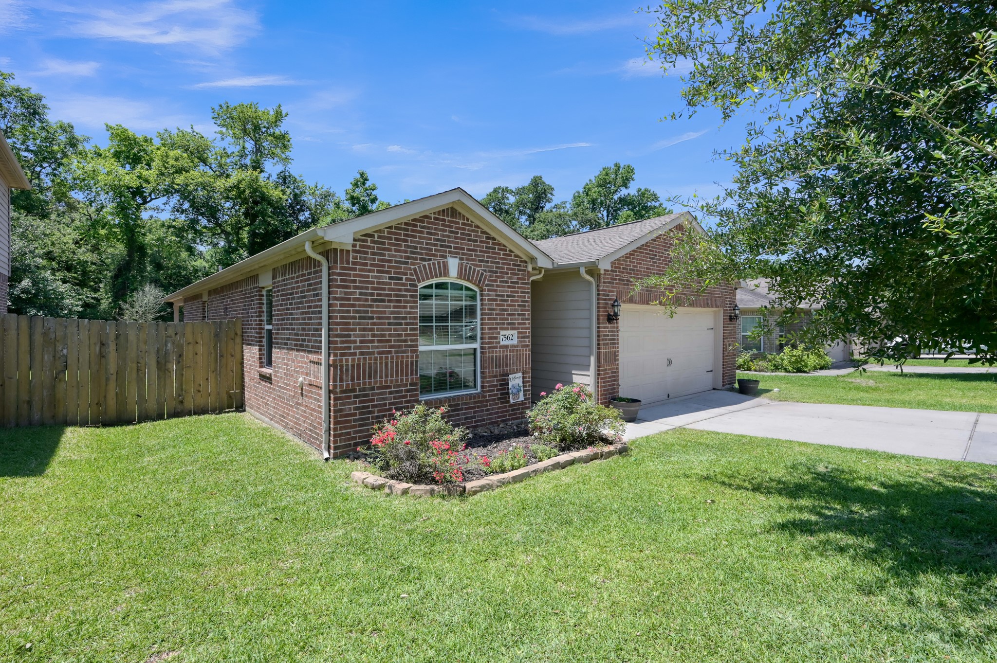7562 Fettle Lane Conroe, TX 77304 - Photo 4 of 30 exterior perspective highlighting the home’s spacious lot, attractive brick façade, and beautifully maintained rose bushes adding charm and curb appeal.
