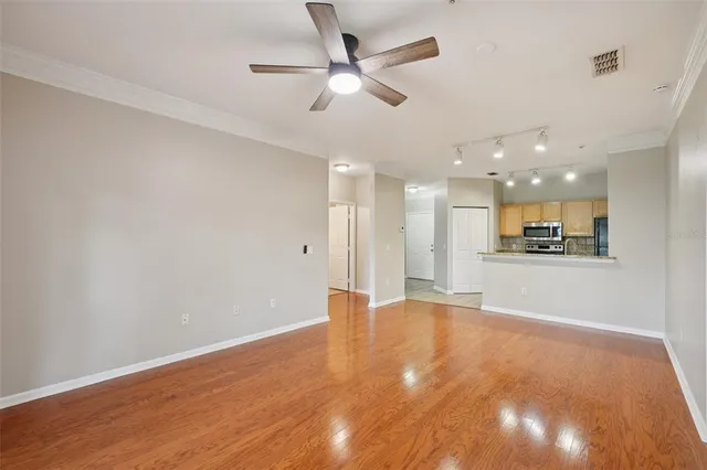 a view of an empty room with kitchen view and wooden floor