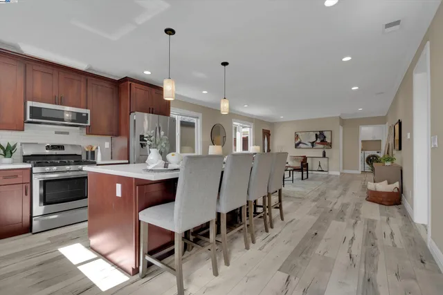 a kitchen with stainless steel appliances granite countertop a stove a refrigerator a kitchen island a dining table and chairs with wooden floor