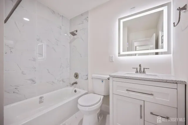 a bathroom with a granite countertop toilet a sink a mirror and a bathtub