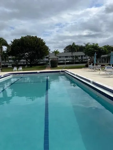 a view of swimming pool with outdoor seating and lots of trees in the background
